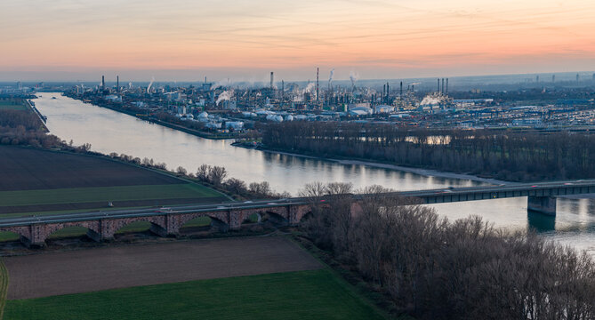 Aerial view of the river reflecting the soft hues of the setting sun, flowing past industrial complexes and bridges, Ludwigshafen am Rhein, Rheinland-Pfalz, Germany.