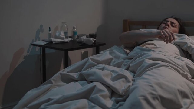 A somber video scene captures a person in bed from a side angle, highlighting a mood of solitude with dim lighting and a cluttered bedside table.