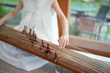 A young girl is playing a long stringed instrument. The instrument is made of wood and has many...