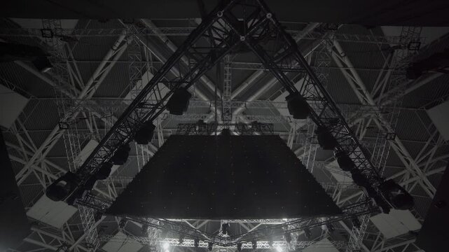 Massive dark LED panel hangs above stage in triangular frame. Grid structure supports lights and forms core of concert equipment setup