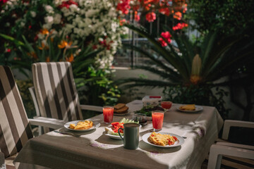 Obraz premium Outdoor breakfast with dishes and drinks on a table surrounded by flowers and plants