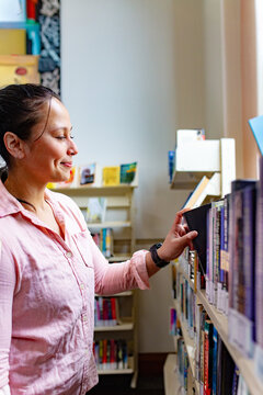 Maori woman studying at a public library looking at book on shelf