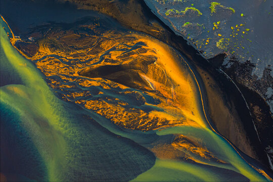 Aerial view of rivers intertwine like golden threads on a dark canvas, creating a mesmerizing tapestry of contrasting hues, Hvolsvllur, Southern Region, Iceland.