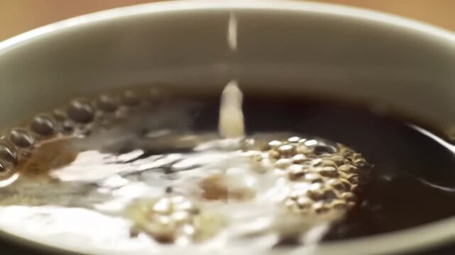 Close-up of milk being poured into a cup of dark, rich coffee.