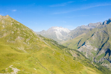 Fototapeta premium Lush grassy slopes and rugged peaks stretch into the distance in the Pyrenees near Gavarnie Gedre. Bright sunlight and crisp air create a sense of freshness and open space in this alpine landscape.