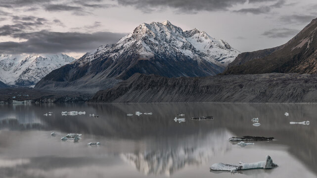 Last light of day at Tasman Glacier with snow-capped mountains, floating icebergs and moody clouds