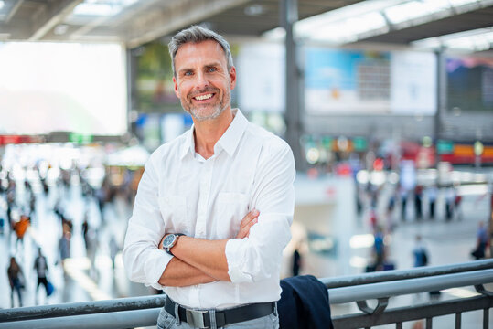 Smiling businessman at train station in white shirt with arms crossed
