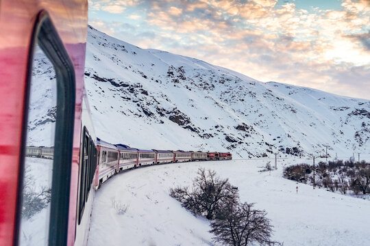 Eastern Express train curving through snowy Erzincan mountains. Features red locomotive, white winter landscape, and scenic window reflections. Iconic Turkish rail journey in Eastern Anatolia.
