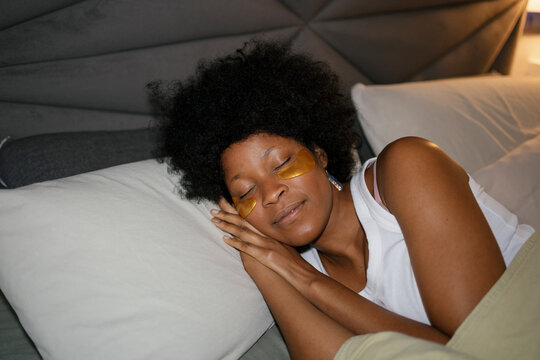 Woman resting in bed with eye patches in cozy evening bedroom