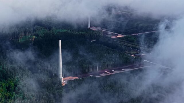 Drone shot showing construction progress of renewable energy wind park through flowing clouds