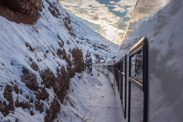 Eastern Express train curving through snowy Erzincan mountains. Features red locomotive, white...