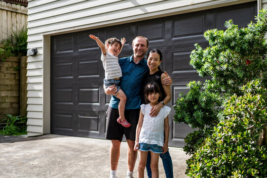 A joyful family of four stands outside their house in an Australian suburb enjoying the sunny day