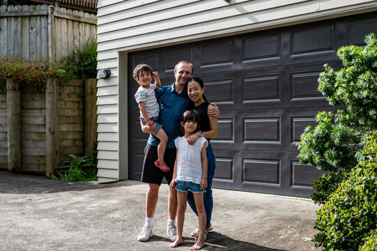 Family stands smiling together outside a house, enjoying their time in a friendly atmosphere.
