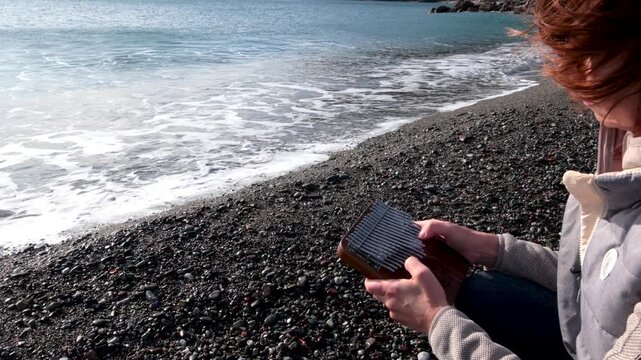 Girl play kalimba by sea. Nature, music, and meditation. Relaxation and mental health. 