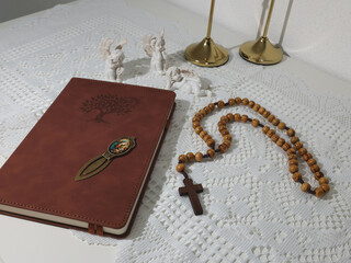 Catholic corner at home. Angel figurine, wooden rosary beads, cross, and prayer book. Faith, symbols, and traditions.