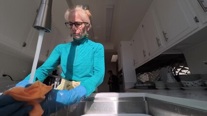 Mature woman carefully washes antique china bowls and plates in a bright kitchen during a sunny day.