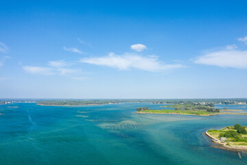 Obraz premium Aerial view of a vivid turquoise estuary with scattered green islets and a wide open sky, capturing the tranquil coastal landscape of Etel in Brittany on a bright summer day.