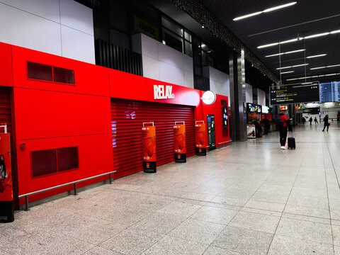 Traveler at a bright red airport Relay storefront with luggage in a busy Krakow airport terminal