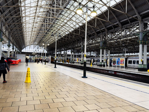 Modern Manchester train station platform with glass roof and passengers waiting for trains