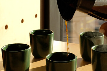 Coffee mugs poured with coffee. Close up pouring black coffee into green ceramic cup, mugs with beautiful steam smoke spins, rising from the cup on wood table