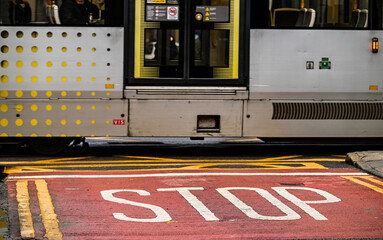Stop line with words STOP ahead of a tram intersection, persons walking across road. 