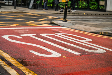 Stop line with words STOP ahead of a tram intersection, persons walking across road. 