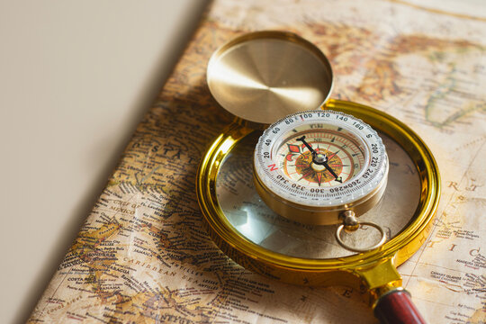 Compass examined through magnifying glass on vintage world map. Concept of travel navigation, strategic planning, business analysis, direction search, exploration and global positioning.