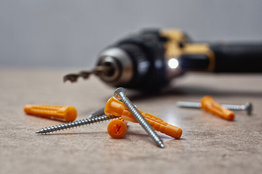 Close up of a cordless drill with a mounted drill bit, metal screws and orange wall plugs on a wooden surface. DIY tools, construction equipment and repair concept.