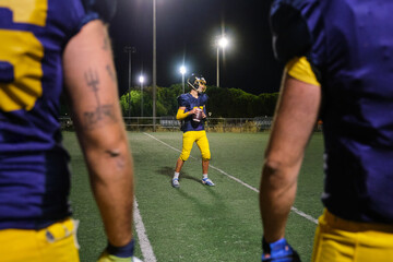 Player standing on an illuminated stadium field at night, holding a football