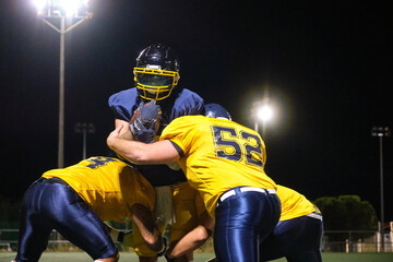 American football players tackling ball carrier on field under stadium lights at night
