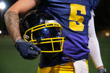American football player holding a helmet with a face mask, wearing a uniform © Ladanifer