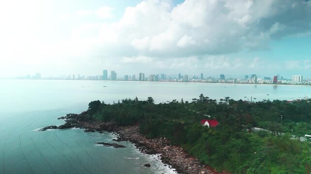 Da nang cityscape stretching along the bay, framed by the lush son tra peninsula coastline with a small white house and rocky beach, presenting a vibrant urban and natural landscape