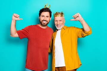 Two men wear crowns and smile together as friends and family in a bright turquoise studio
