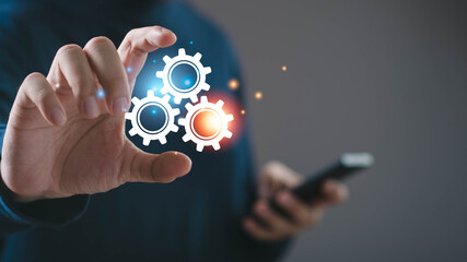 Businessman holding glowing gear icons with smartphone representing mobile system, workflow automation, app configuration, digital integration, smart technology, software management, modern business.