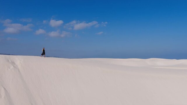 A solitary figure traverses a vast white sand dune under a clear blue sky on Socotra Island