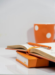 There is an orange pen on the diary, against the background of an orange mug, and there is space for text.