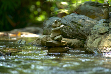 A Zen symbol in the form of a stone pyramid stands majestically in the middle of a river amidst a lush natural forest.