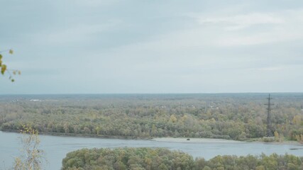river horizon distant forest overcast sky, slow panoramic reveal from leafy hilltop overlooking winding river and marsh islands, mixed deciduous canopy in soft autumn tones, calm reflective water,