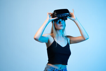 Confident woman wearing virtual reality headset, modern VR technology portrait with immersive digital experience on blue studio background