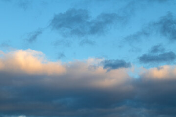 Obraz premium Dramatic evening sky with a layer of dark, heavy clouds illuminated by a soft golden glow. Natural blue sky background with scattered clouds.