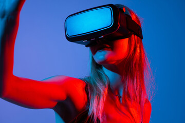 Close-up of woman wearing VR headset and raising arm in virtual space, immersive technology with neon red and blue lighting