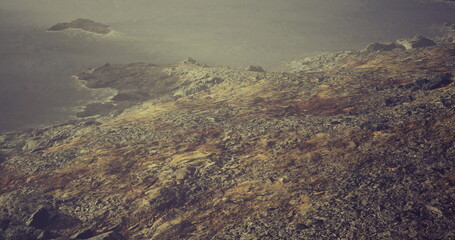 Naklejka premium aerial rugged coastline under muted haze, expansive rocky shore descending into calm sea, distant islets dotting horizon, soft golden light casting sepia tones,