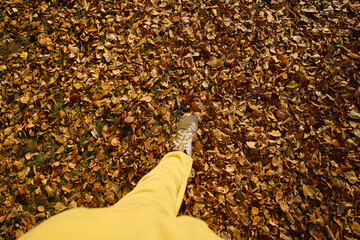 A person in yellow pants walks on a thick layer of colorful autumn leaves