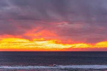 Orange sunset with storm clouds over calm ocean