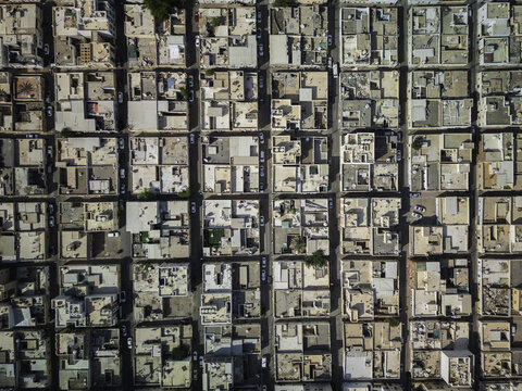 Aerial view of closely packed buildings create a uniform grid pattern broken by narrow streets, revealing subtle variations in texture and tone, Muscat, Oman