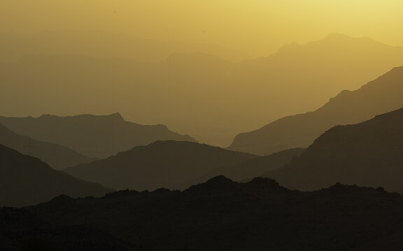 Aerial view of the rugged mountain ranges painted in hues of gold and umber under a hazy sky, Muscat, Oman