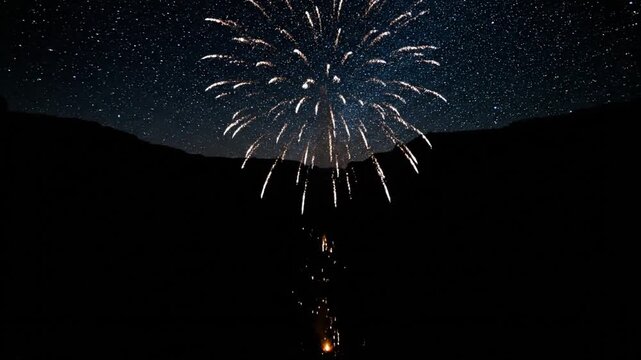 A breathtaking display features fireworks exploding and a fiery "firefall" spectacle cascading down dark canyon walls beneath an epic, star-filled night sky.