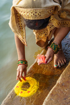 India. Uttar Pradesh State. Varanasi. A richly adorned young Hindu pilgrim, dressed in a golden sari, makes a ritual offering of haldi (turmeric) powder during the Diwali celebrations