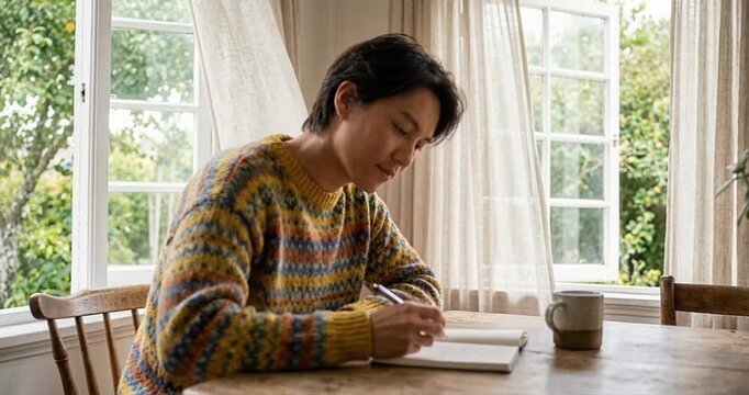 Person writing in notebook at table near windows interior
