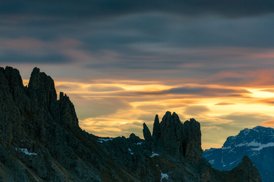 Aerial view of jagged peaks cutting through a dramatic sunset sky, casting long shadows across the rocky terrain, Fassa valley, Trentino-South Tyrol, Italy.